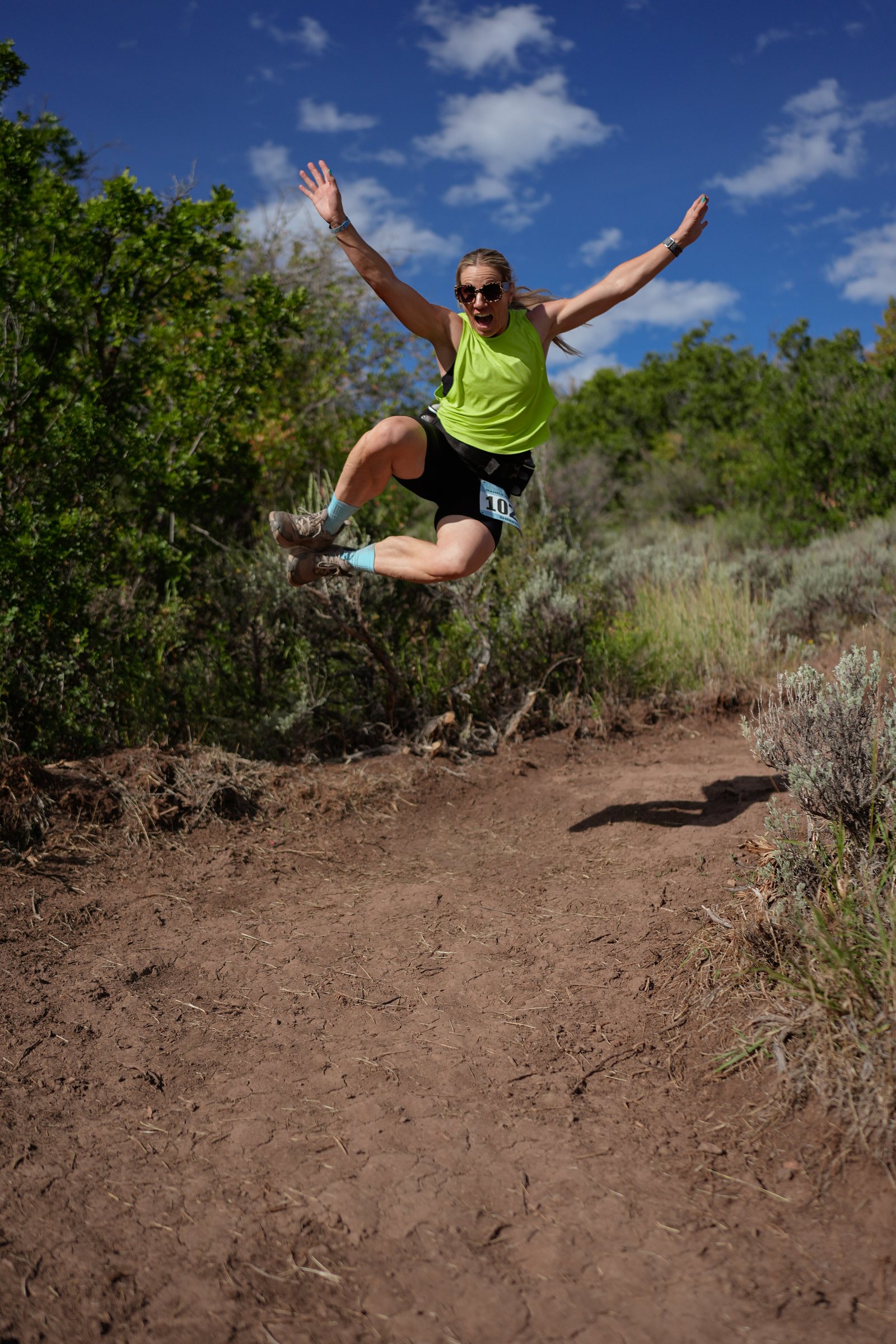 A runner leaping off the trail mid stride, arms wide.