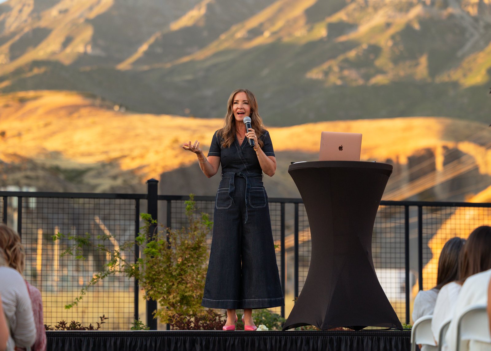 The VIP dinner keynote on stage as the Wasatch range turns gold behind her.